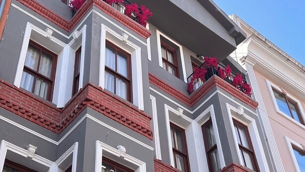 Um edifício de vários andares com entrada na esquina, grandes janelas e detalhes em tijolos vermelhos.