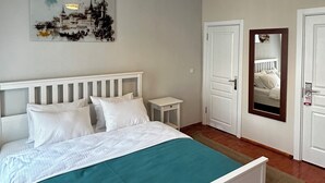 Quarto com cama, mesa de cabeceira, espelho fixado na parede e luminária de teto.