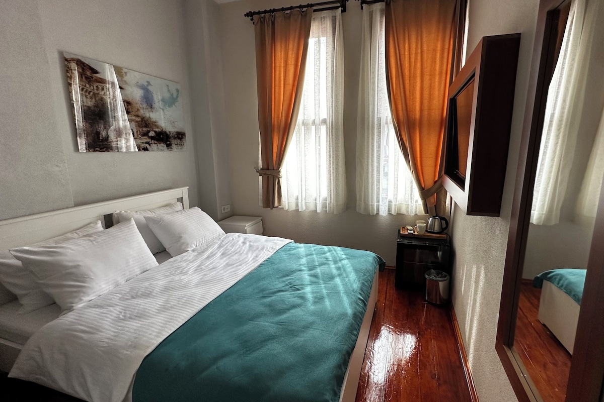 A bedroom with a bed, a bedside table, a mirror, and a window with curtains.