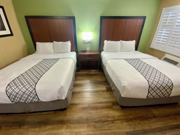 Une chambre d’hôtel avec deux lits, une table de chevet, une lampe fixée au mur et une fenêtre avec des stores.