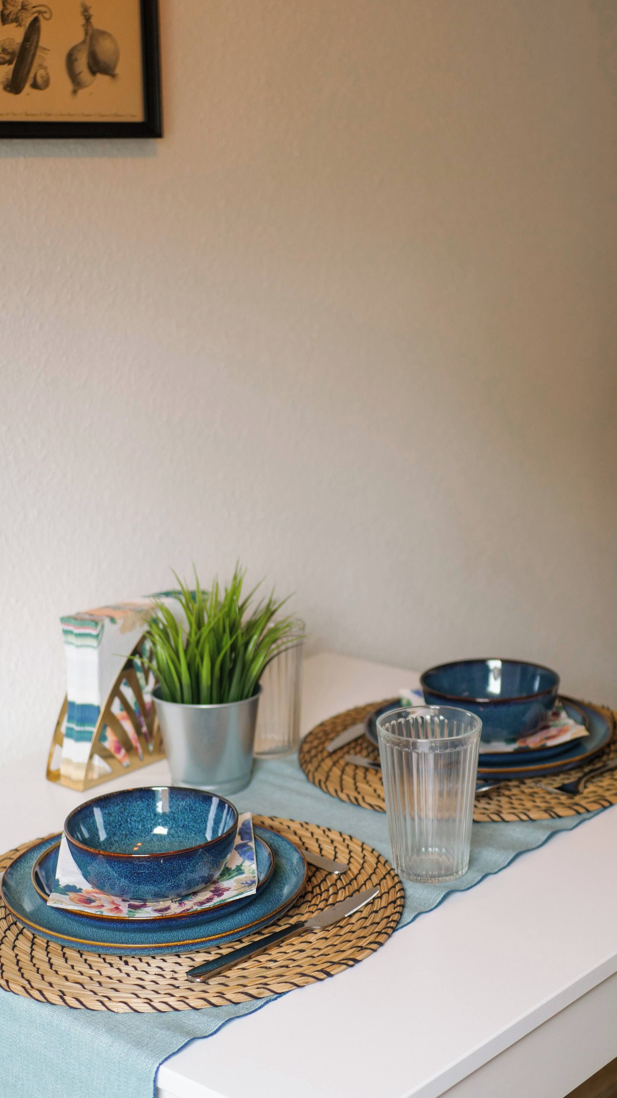 Ein Tisch mit blauen Schüsseln, einem klaren Glas und gewebten Unterlays.