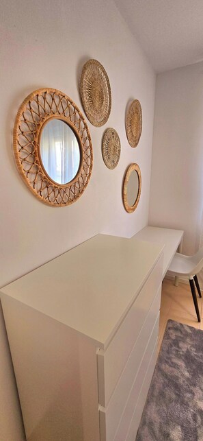 Ein Zimmer mit einem weißen Schminktisch, einem Spiegel mit Korbflechtrahmen und mehreren Wanddekorationen aus Bändern.