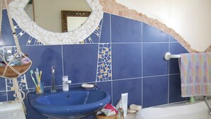 A bathroom with a blue sink, a white bathtub, and a mirror above the sink. - Single-story house in the countryside (Plogonnec)