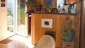 A kitchen with wooden cabinets, a dining area with a chair, and a view through a glass door. - Single-story house in the countryside (Plogonnec)