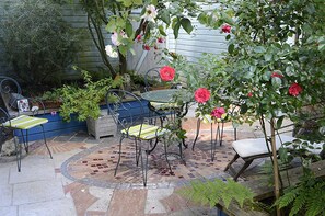 Eine Außenpatio mit einem Mosaikboden, Metallstühlen, einem Tisch und einem Rosenbusch.