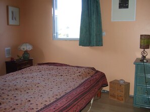 Ein Schlafzimmer mit einem Bett, einem Schminktisch, einer Lampe und einem Fenster mit Vorhang.