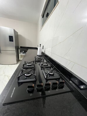 A kitchen with a black stove top, a refrigerator, and white tiled walls. - Modern Ocean View Villa with Private Pool (Ilhéus)