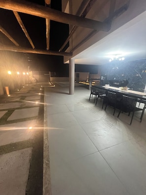 An outdoor dining area with a long table and chairs, under a covered structure with exposed beams. - Modern Ocean View Villa with Private Pool (Ilhéus)