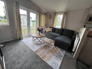A living room with a grey sofa, a round coffee table, and a patterned rug. - Clear Water Holidays (Northampton)
