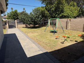 A backyard with a brick pathway, a swing set, and a seesaw. - 3-bedroom house in perfect Los Angeles with cool AC and pool (Los Angeles)