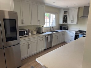 A modern kitchen with stainless steel appliances, white cabinetry, and a window providing natural light. - 3-bedroom house in perfect Los Angeles with cool AC and pool (Los Angeles)