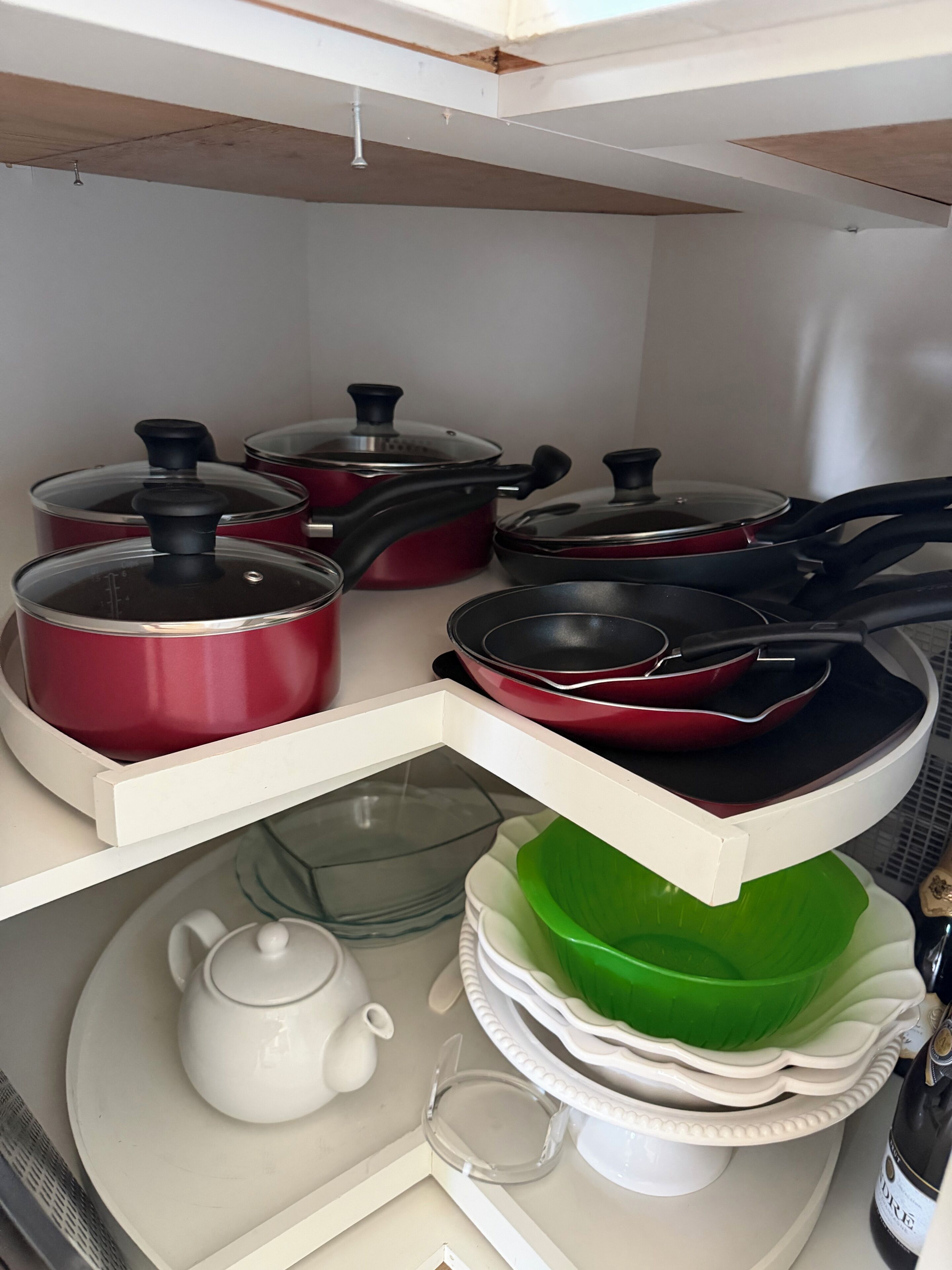 Una cocina con ollas y sartenes en estantes blancos, un tetera y un tazón verde sobre un plato blanco.