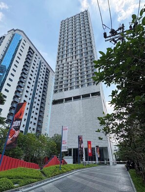 A modern building with a glass facade, a red-brick entrance, and a sign indicating a sales gallery. - Duplex 1-bedroom Apartment in Thonglor, Bangkok (Bangkok)