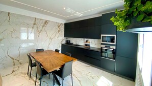 A modern kitchen with dark cabinets, a wooden dining table, and a built-in oven. - Vrbo Property (Castel Bolognese)