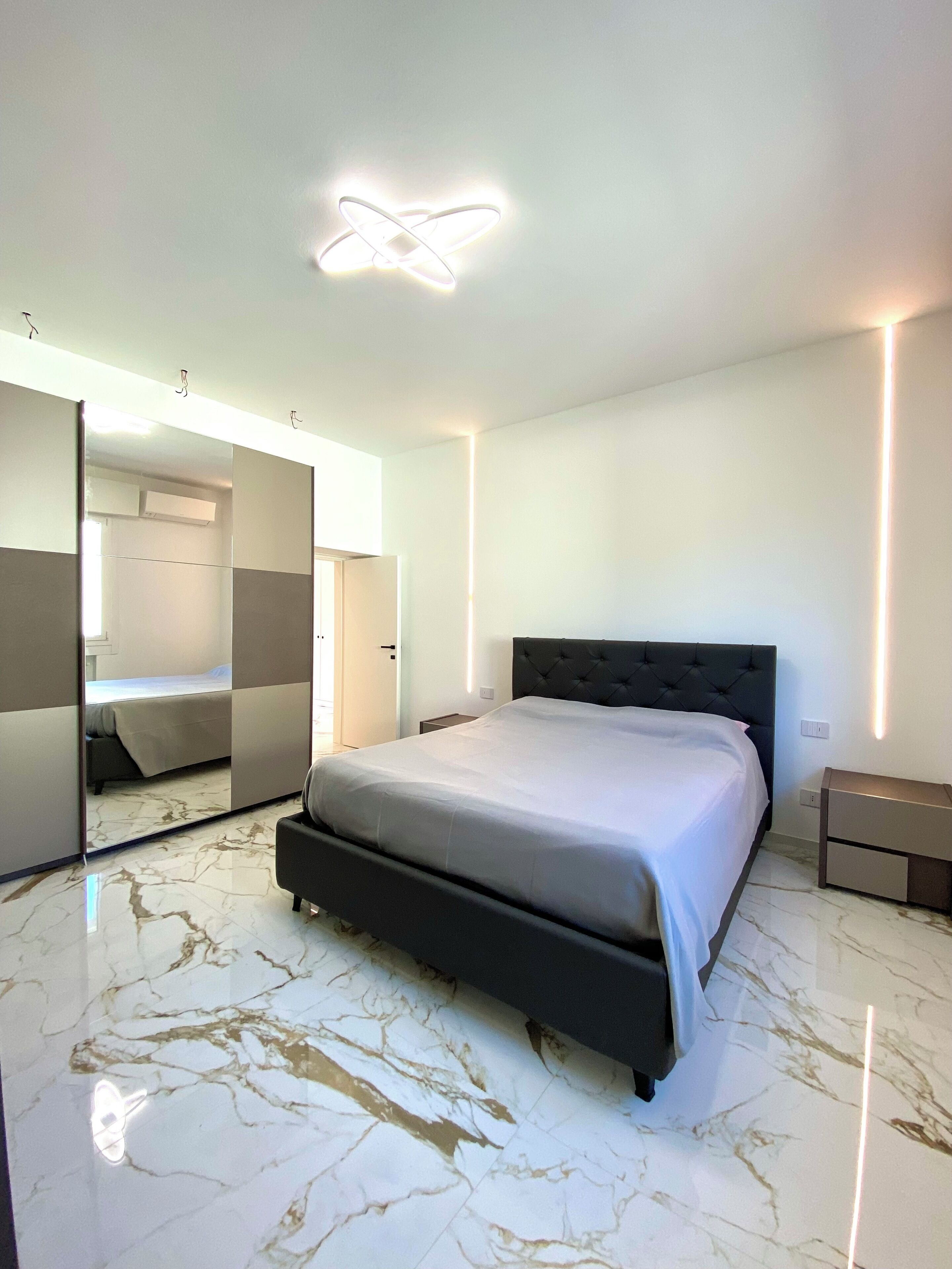 A modern bedroom with a large bed, a built-in wardrobe, and a mirror.