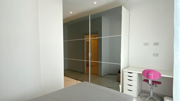 A modern bedroom with a bed, a desk with a chair, a wardrobe, and a mirror.