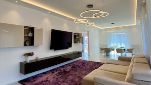 A modern living room with a flat-screen TV, a sofa, a purple rug, and a dining area in the background. - Vrbo Property (Castel Bolognese)
