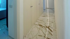 A hallway with a marble floor, white walls, and a door leading to a room with a bed.