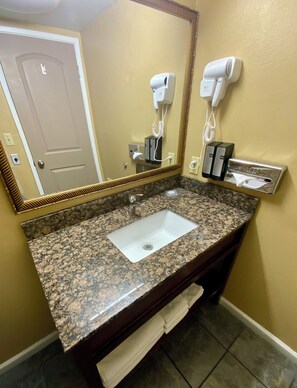 A bathroom with a granite countertop sink, a mirror, a hairdryer, and a towel rack. - Cozy 3 Queen Suite 131–Stroll Historic Downtown Great Restaurants & Unique Shops (Grants Pass)
