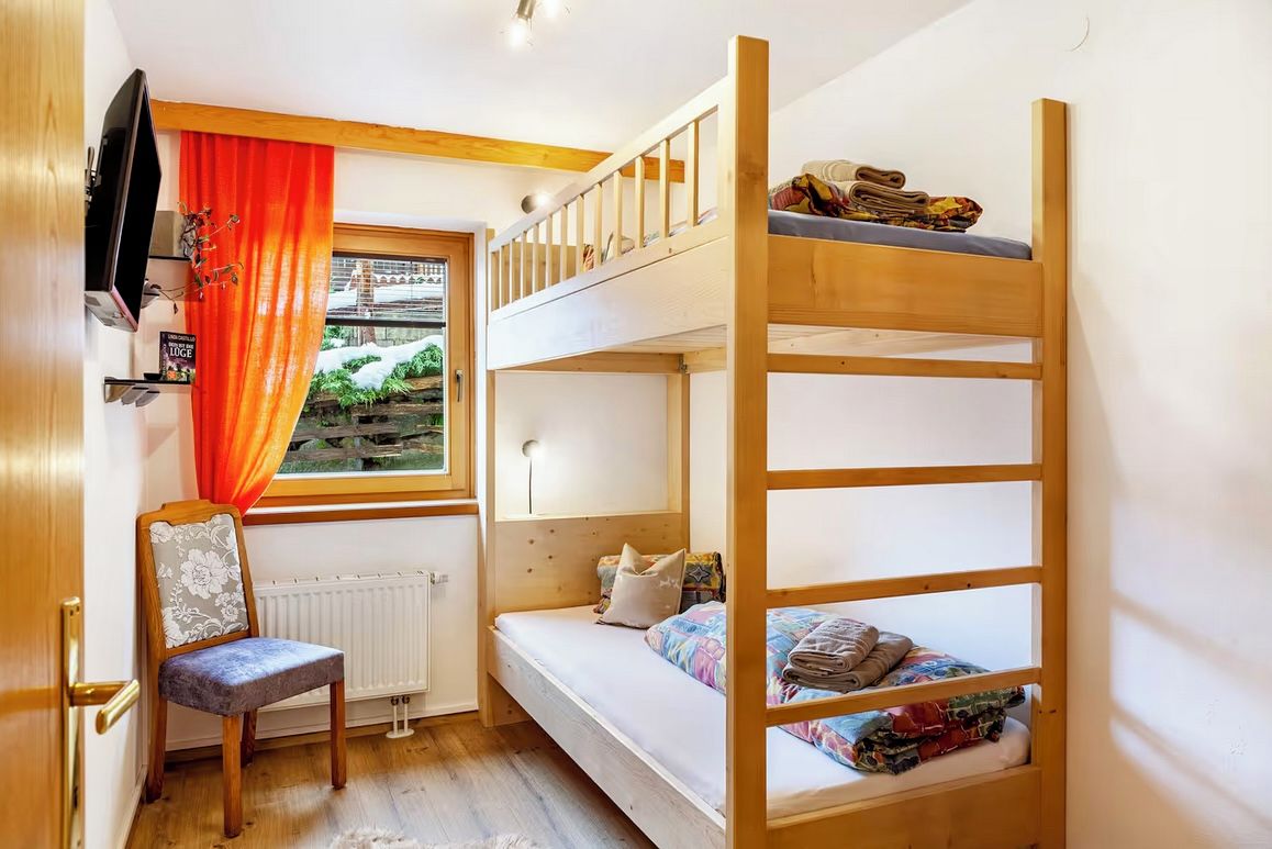A bunk bed room with a window, a chair, and a radiator.