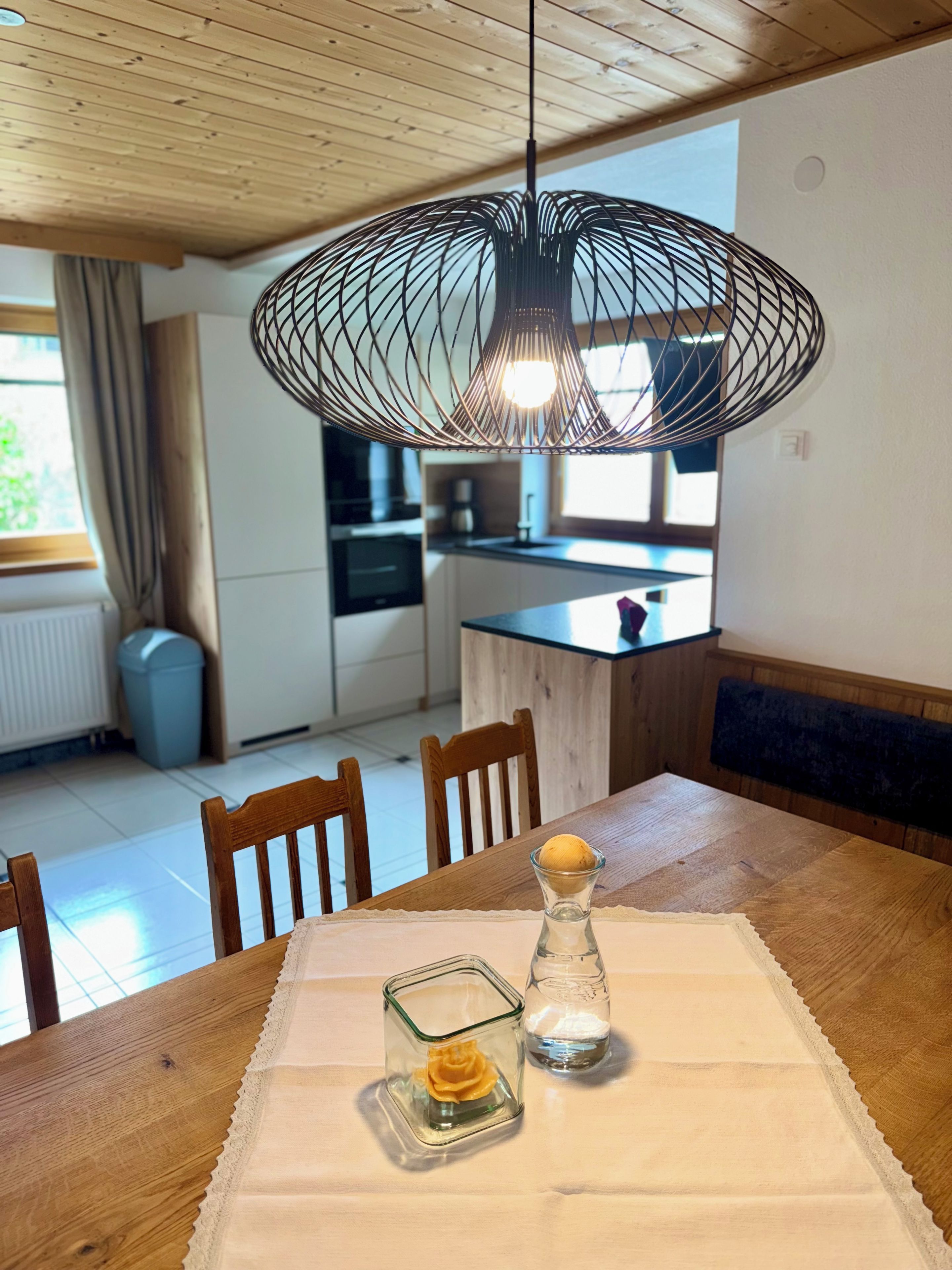 Un coin repas avec une table en bois, des chaises, un porte-bougie en verre et une suspension.
