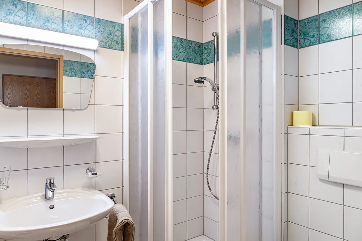 A bathroom with a shower, sink, mirror, and a towel rack.