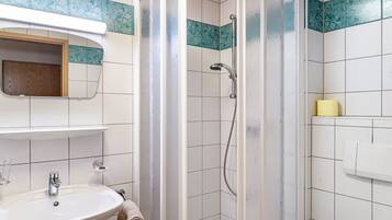 Un baño con ducha, lavamanos, espejo y toallero.