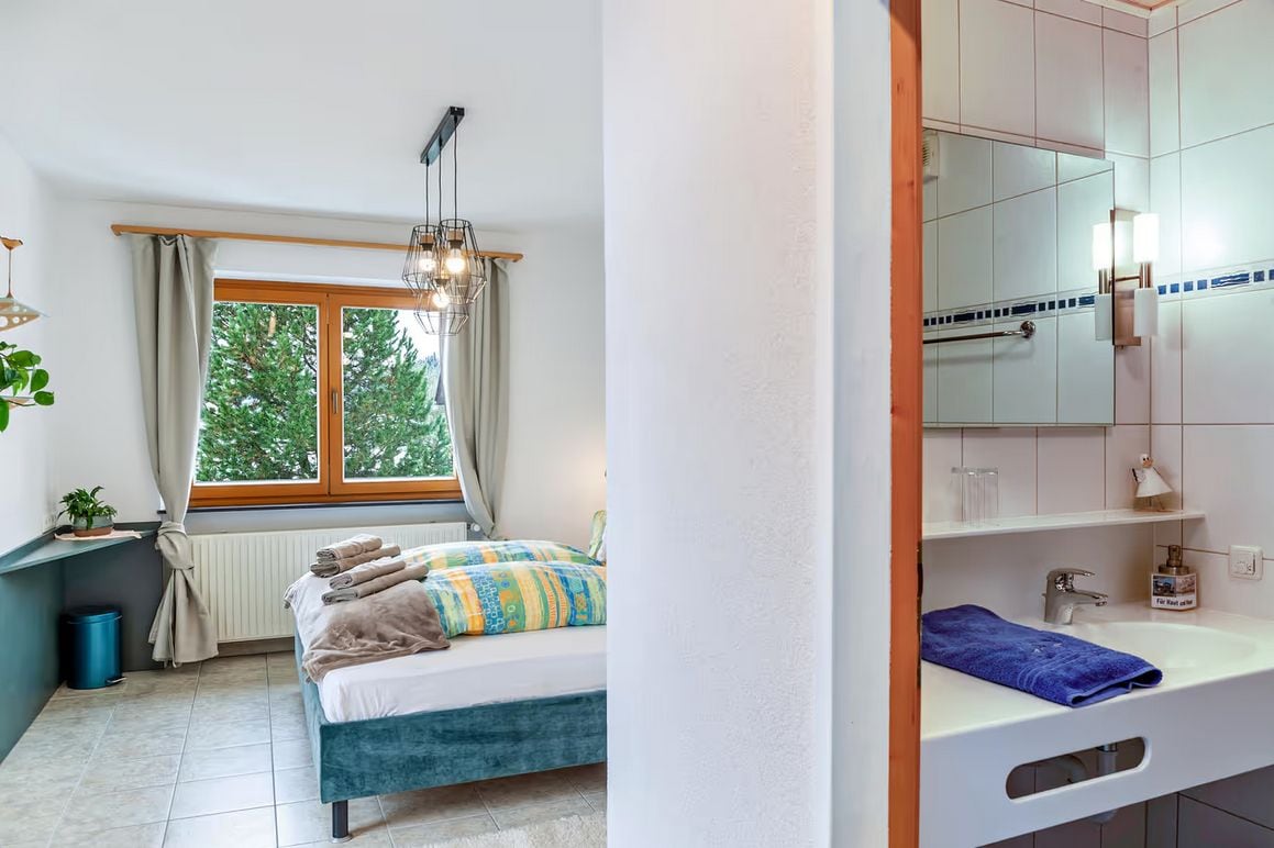 Un dormitorio con cama, ventana y baño con lavamanos y espejo.