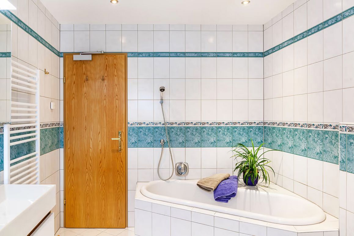 A bathroom with a wooden door, a white bathtub, a shower, and a potted plant.