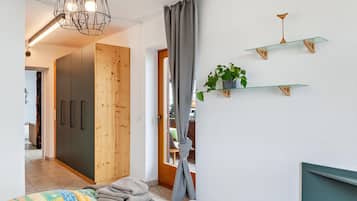 Een slaapkamer met een bed, een kledingkast, een hanglamp, een raam met gordijnen en een wandplank met een plant.
