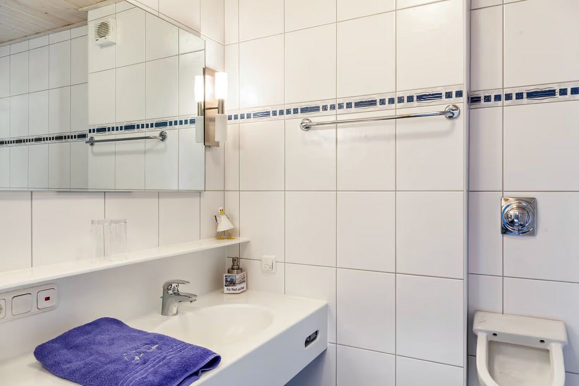 Ein Badezimmer mit einem weißen Waschbecken, einem Spiegel, einem Handtuch, einer Haltestange und einer Toilette.