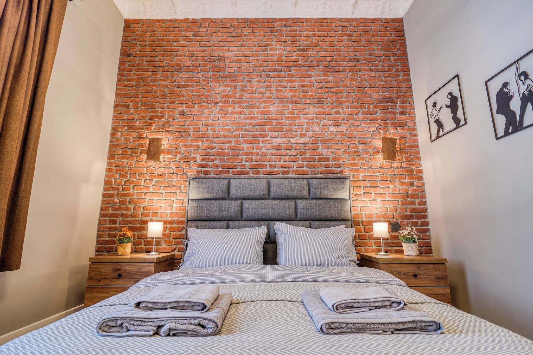A bed with a brick wall backdrop, two bedside tables with lamps, and a headboard.