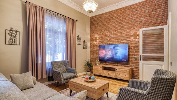Una sala de estar con un sofá, sillones, una mesa de centro, un televisor y una pared de ladrillo.