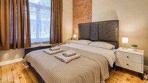 Un dormitorio con pared de ladrillo, una cama con cabecero, una mesita de noche, una lámpara y una ventana con cortinas.