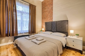 A bedroom with a brick wall, a bed with a headboard, a nightstand, a lamp, and a window with curtains. - Premium House, 3BR, Renovated, Best Loc Kadıköy (Kadıköy)