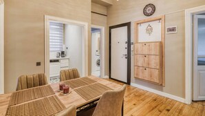 Un comedor con mesa de madera, sillas y posavasos. Se observa una puerta con panel decorativo y un reloj en la pared.