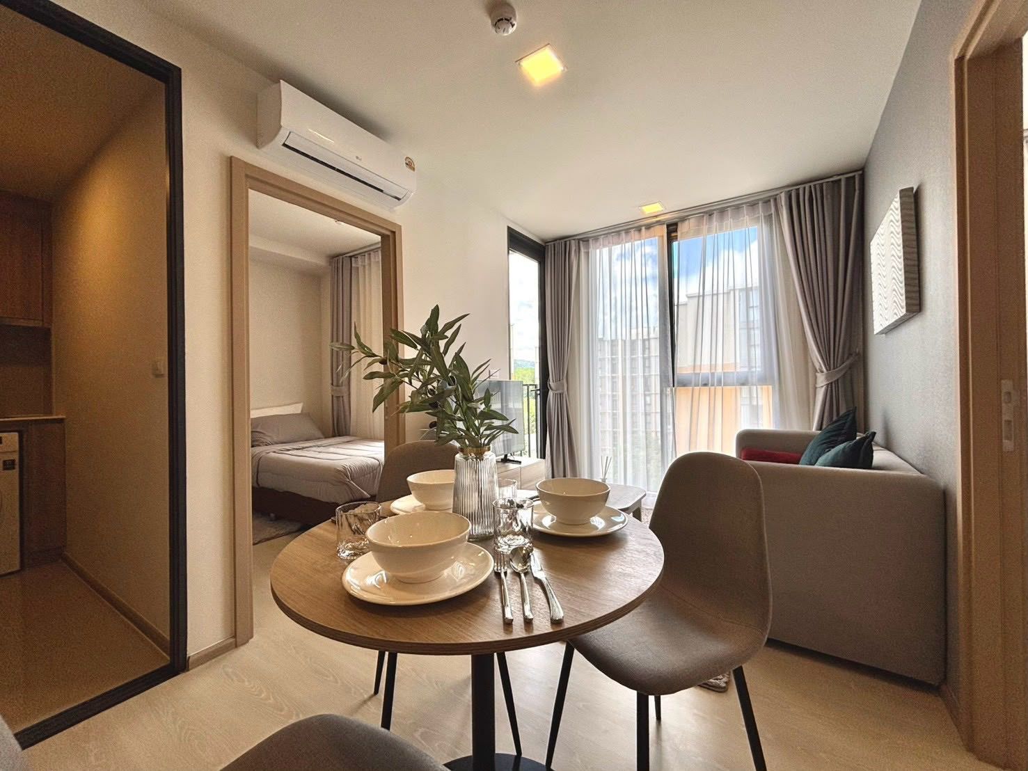 Habitación moderna y luminosa con mesa de comedor para dos personas, un sofá y una cama al fondo.