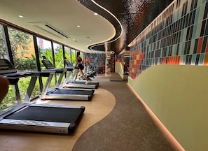Een sportschool met loopbanden, een persoon die aan het sporten is, en een muur met kleurrijke tegels.