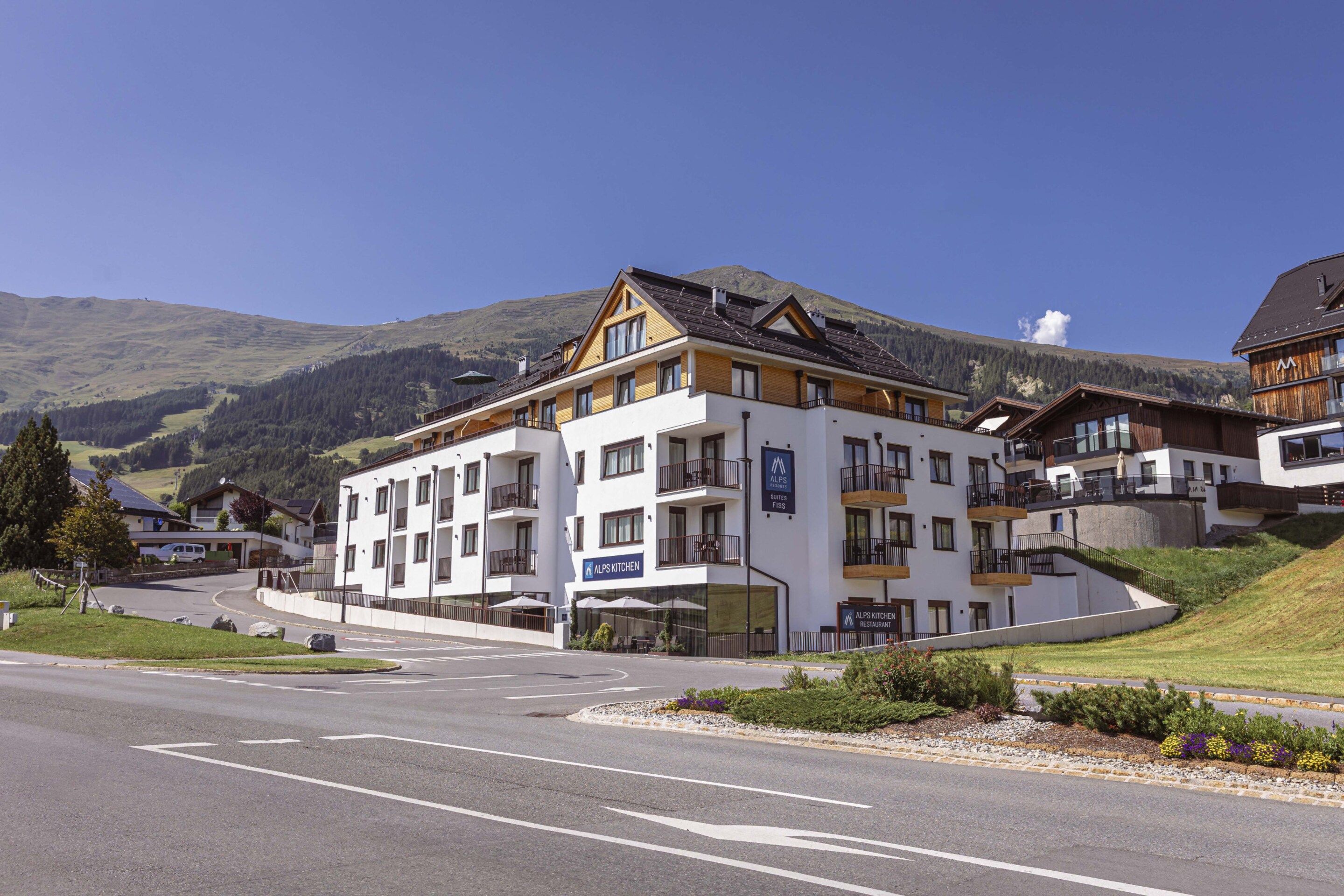 A multi-story hotel with balconies, a restaurant, and a sign for 'ALPS KITCHEN.'