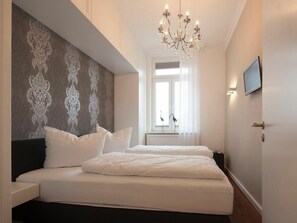 Ein Schlafzimmer mit einem großen Bett, einer Chandelüster, einem an der Wand befestigten Fernseher und einem Fenster, vor dem sich zwei Vögel befinden.
