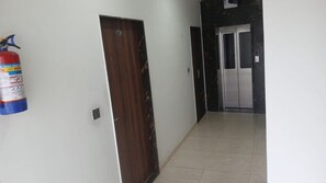 A hallway with a fire extinguisher mounted on the wall, a wooden door, and an elevator. - Deluxe Restaurant Inn (Faizabad)