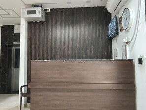 A reception desk with a dark wood finish, a clock, and a 'No Smoking' sign on the wall. - Deluxe Restaurant Inn (Faizabad)