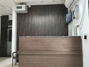 A reception desk with a wooden finish, a clock, and a no smoking sign on the wall. - Deluxe Restaurant Inn (Faizabad)