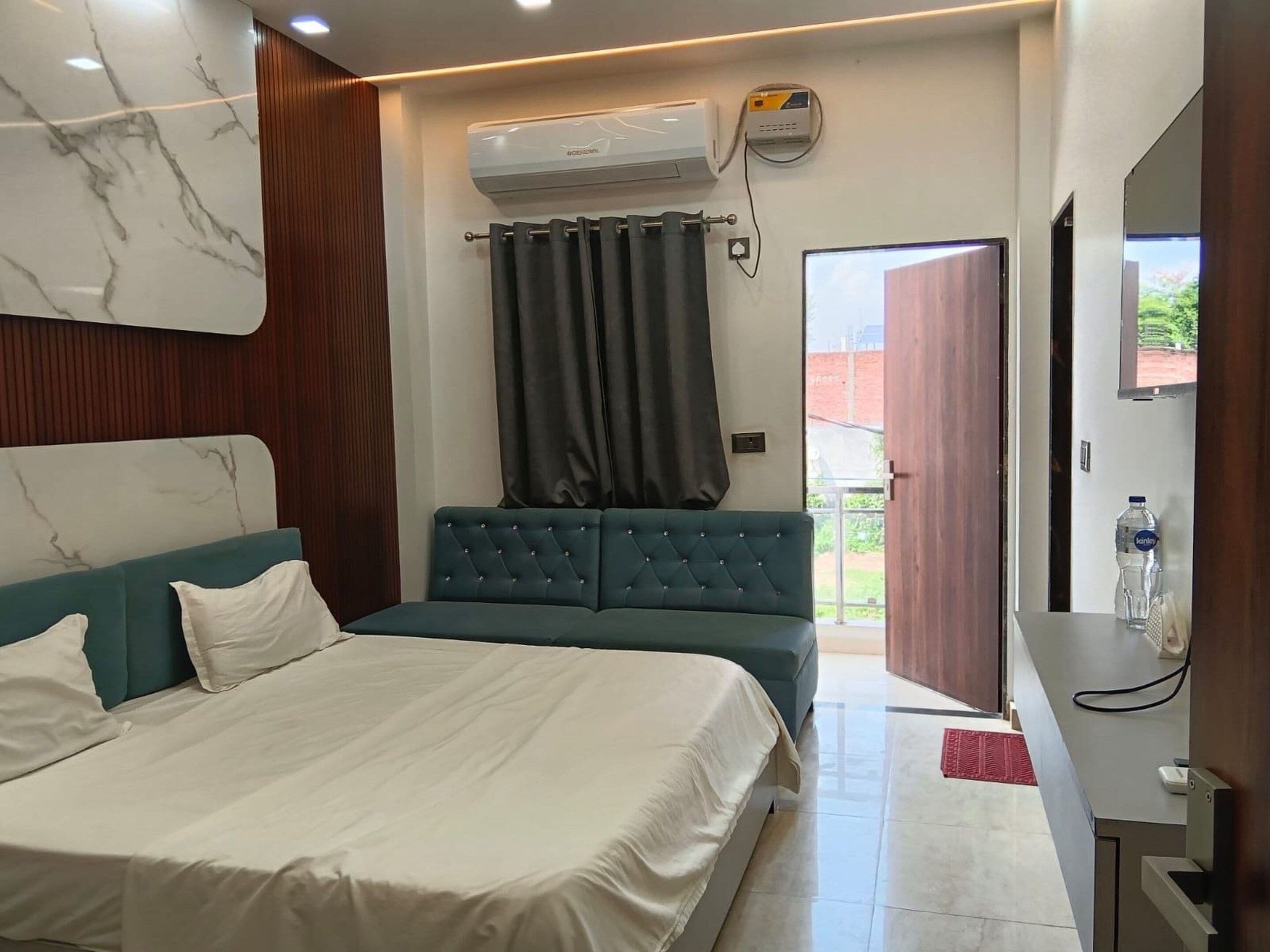A modern bedroom with a bed, a seating area, a TV, and an air conditioning unit.