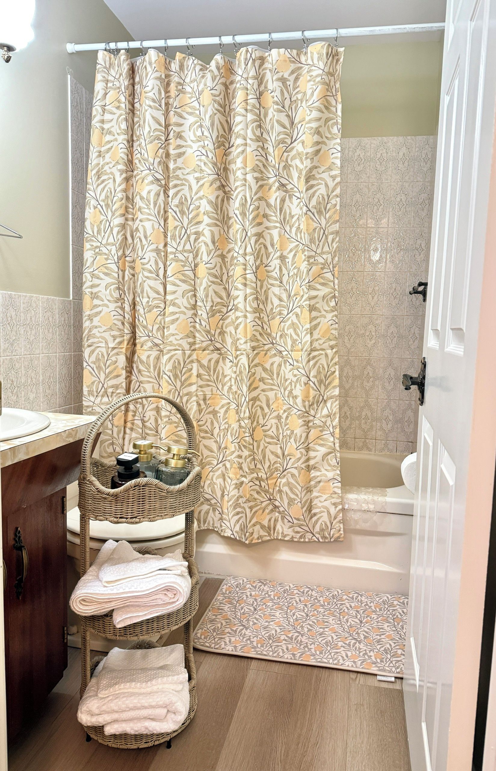 Une salle de bain avec un rideau de douche, un panier en osier contenant des serviettes, une baignoire et un petit tapis.
