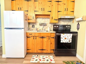 Une cuisine avec des meubles de rangement en bois, un réfrigérateur blanc, une cuisinière noire et un tapis à motifs.