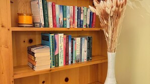 Una libreria in legno con libri e un vaso con fiori secchi.