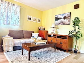 Un salon comprenant un canapé, une table basse, un meuble, une lampe, une plante en pot et un tableau accroché au mur.