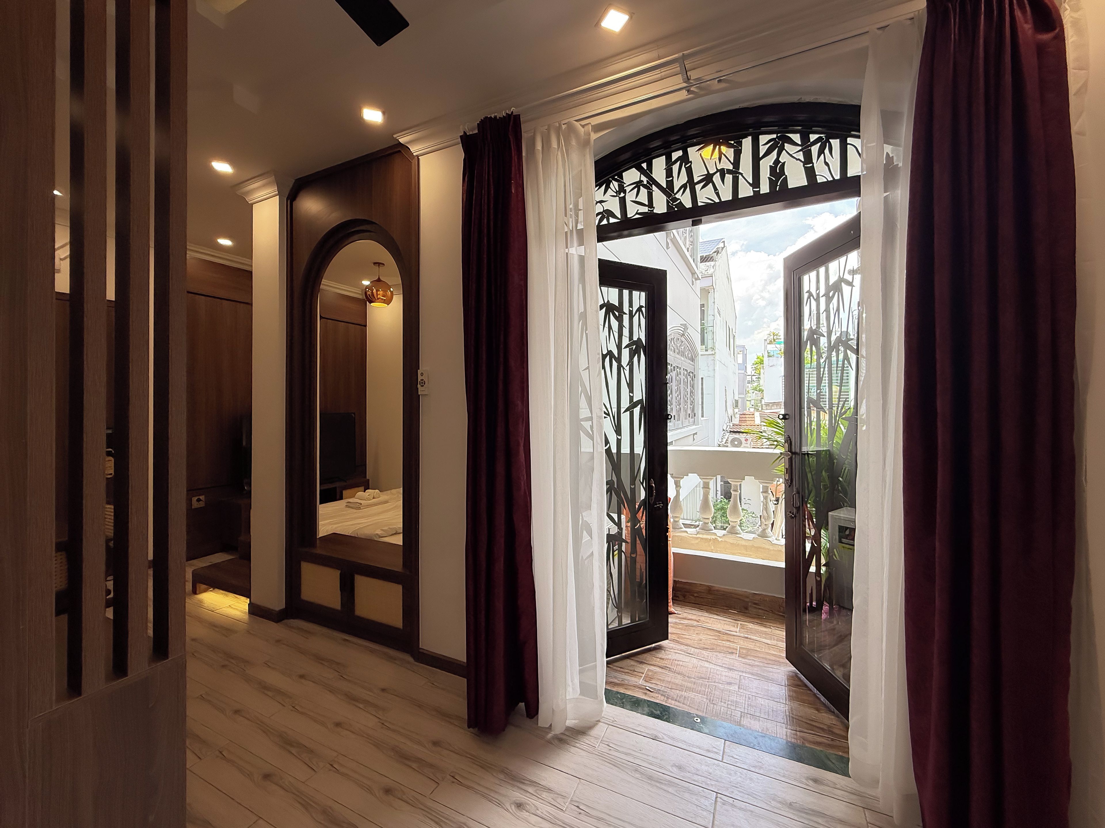 A hotel room with a wooden floor, a bed, a wardrobe, and a balcony with a view of the city.