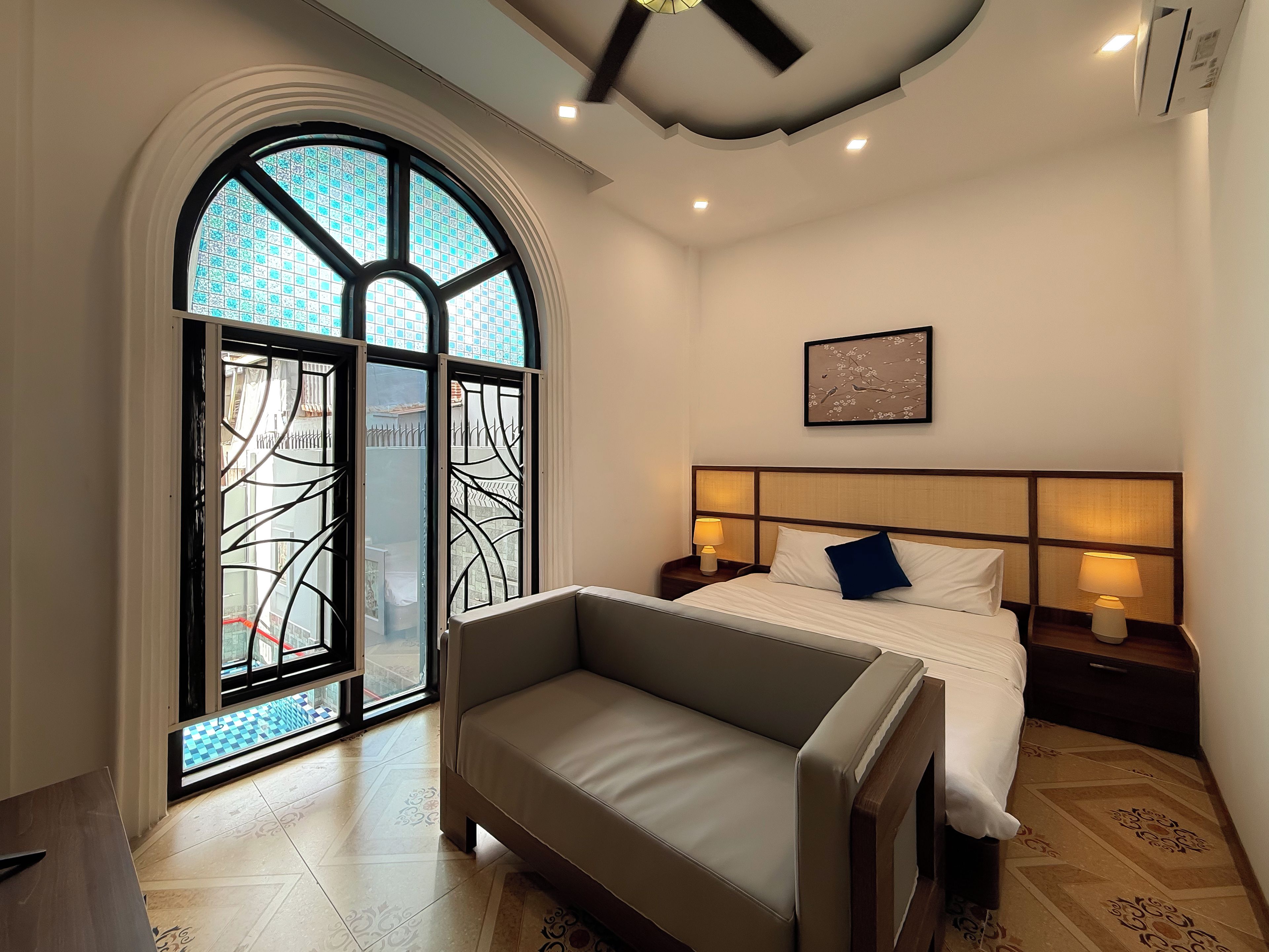Habitació d'hotel amb un llit, un sofà, una gran finestra d'arc i un ventilador de sostre.